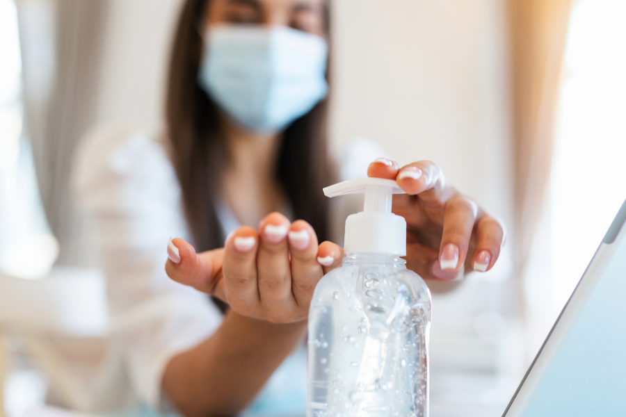 An employee using hand sanitizer at a dispenser in an office setting; one of many best practices for office germ prevention